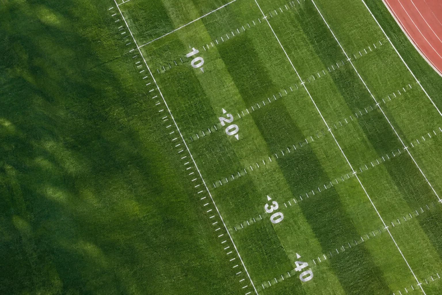 An overhead view of a green football field with geometric yard lines in morning light